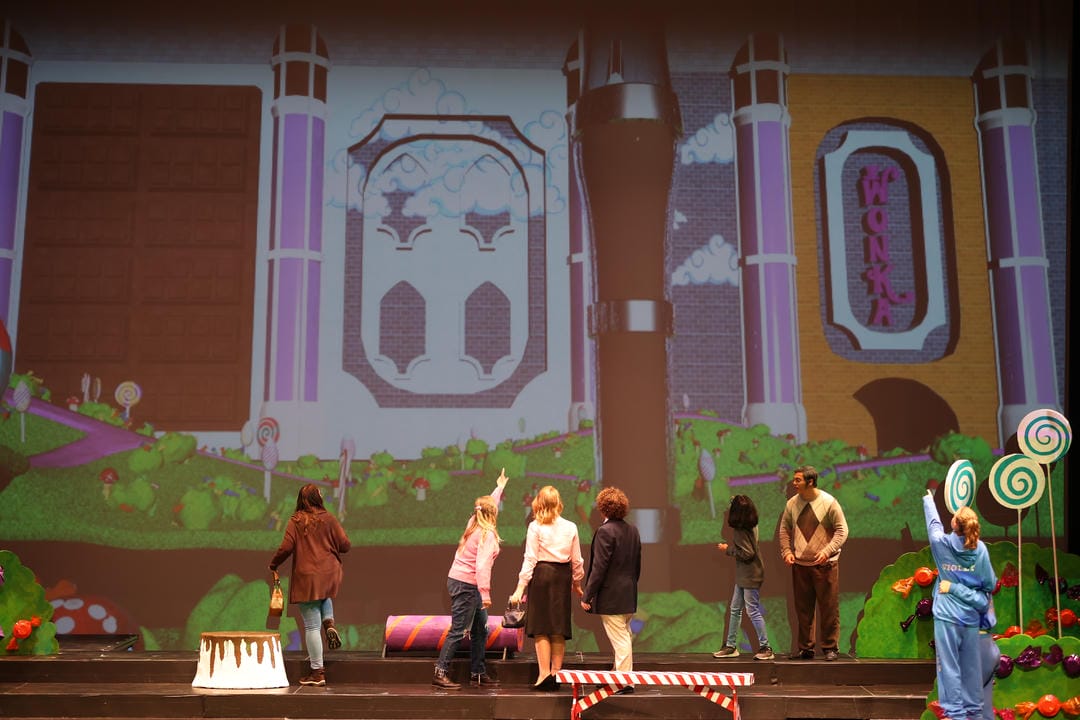 Augustus Gloop being sucked up by a chocolate tube as other characters watch in horror.