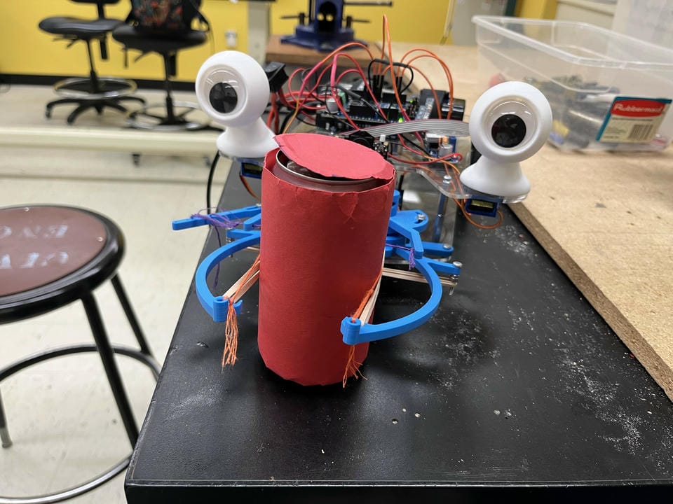 The front of the rover, grabbing a red can with its claw.