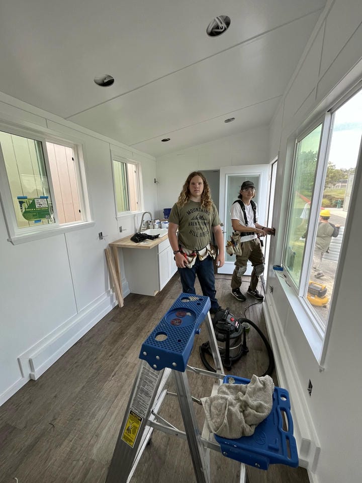 Two students are in the tiny house working, with much of the interior finished.