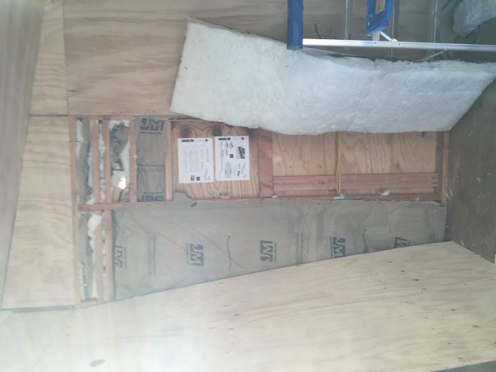 A plywood panel is removed from the wall, exposing insulation and cables.